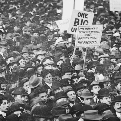 Vintage photo of a massive assembly of workers protesting with signs for the IWW ('One Big Union') and against war ('the workers fight wars … the bosses reap the profits').