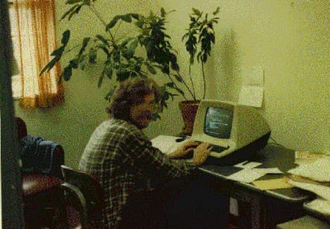 Stephen Daniel, seated at his computer terminal, looks back over his shoulder as his picture is being taken.